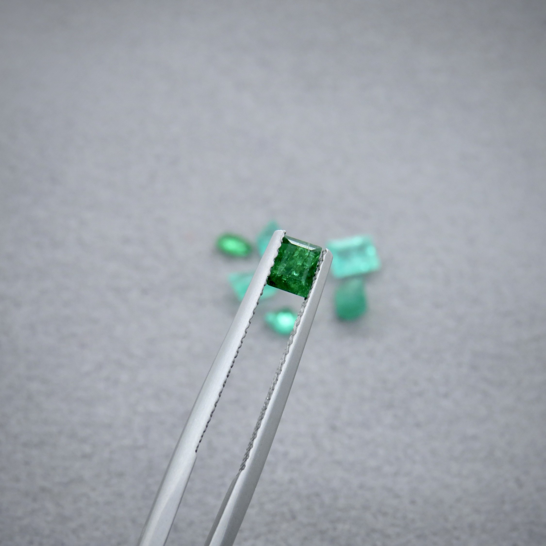 Tweezers holding a square green stone